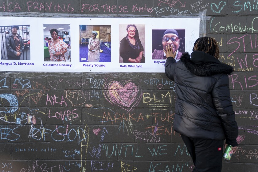 A mourner places her hand on a collection of photos on a wall covered in messages and names