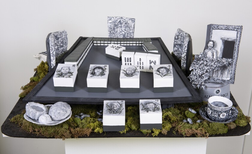 An altar features black and white drawings of people's faces with sculptural renderings of food and other objects.