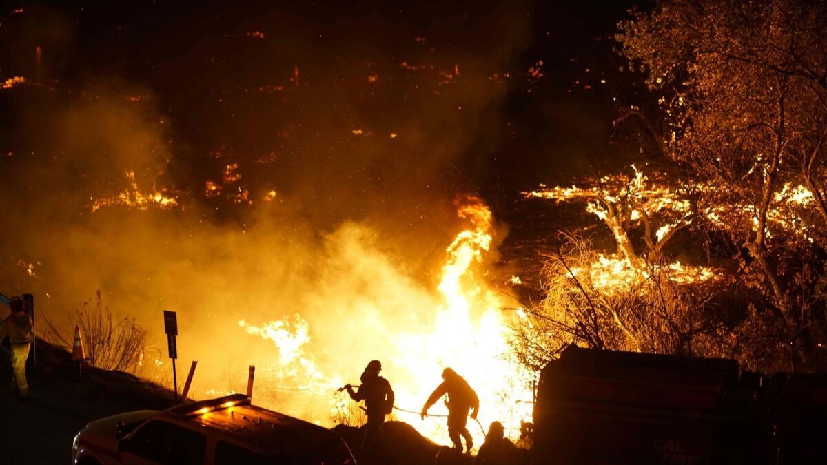 Firefighters battle the Lilac Fire in Bonsall in December 2017. The Moody's Investors Service this month downgraded all three investor-owned utilities in California over concerns about wildfire liability costs.