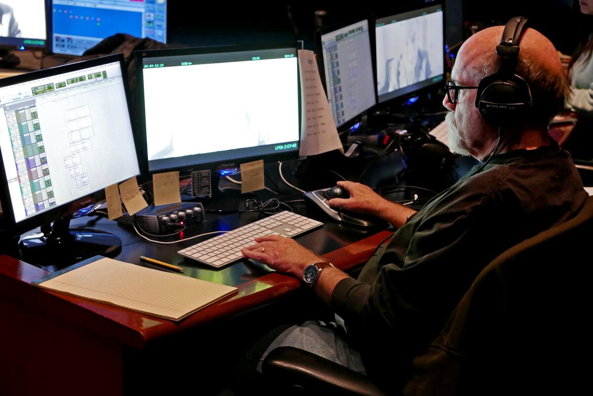 A man wearing headphones works on two computer screens.
