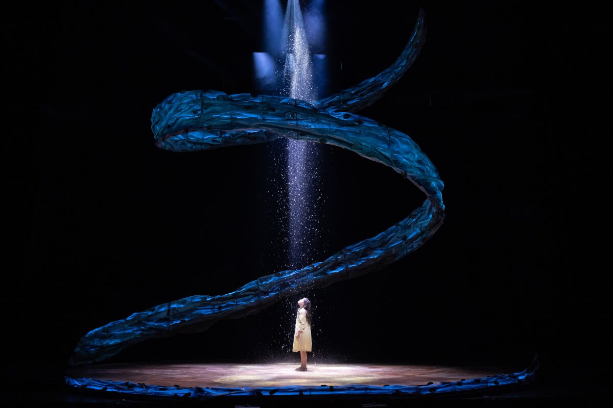 A young girl looks up at falling rain in a stage production