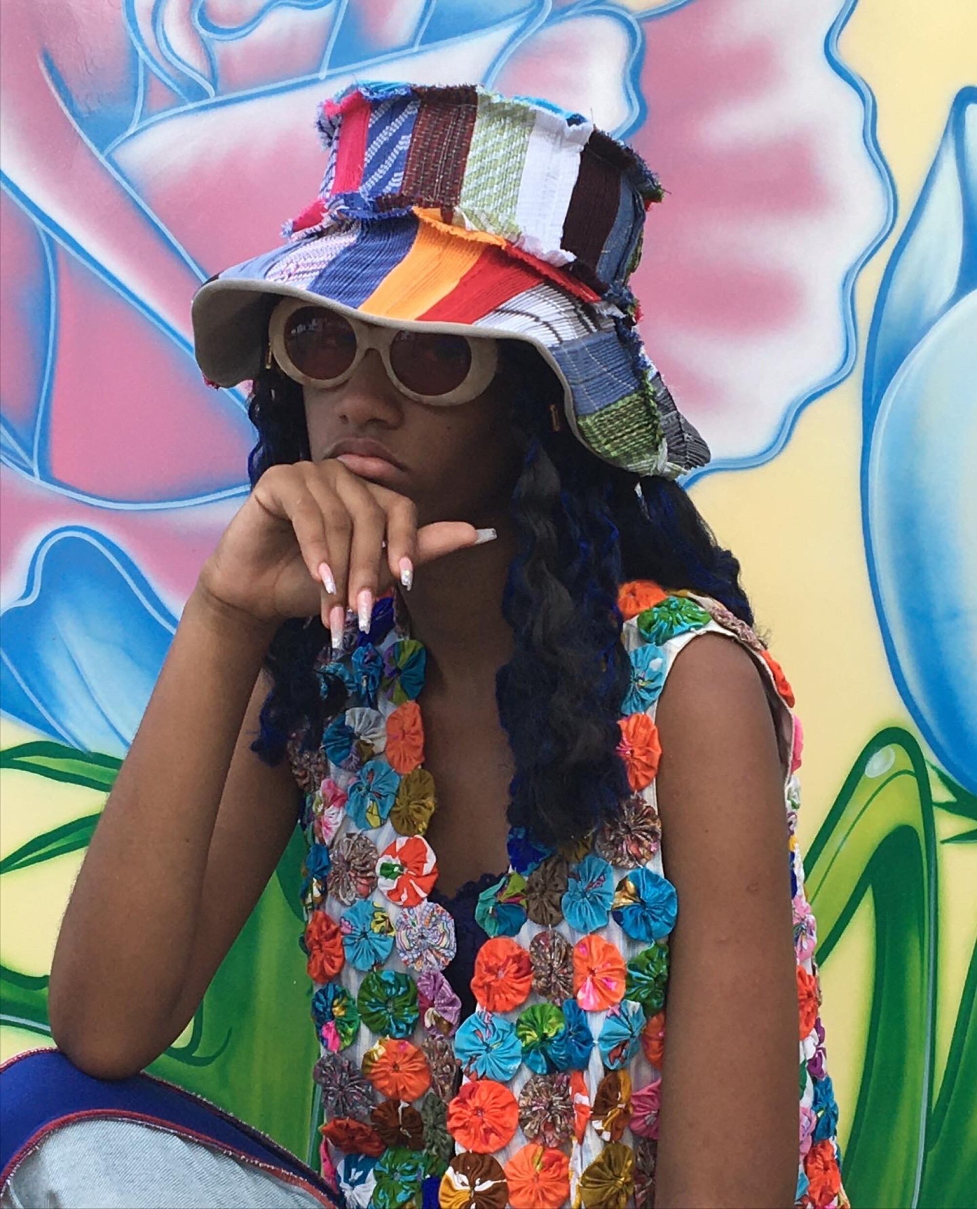A woman wearing chunky white-framed sunglasses and a colorful bucket hat and blouse.