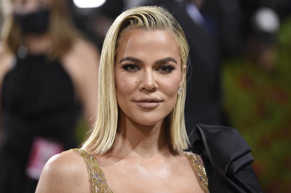 Khloe Kardashian looks directly ahead in a metallic dress with her blond hair slicked over to one side