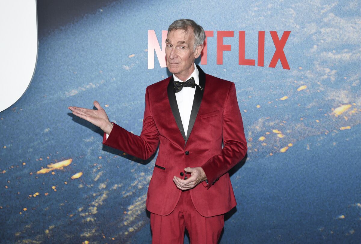 A man in a bright red velvet tuxedo gestures with one arm in front of a Netflix backdrop.