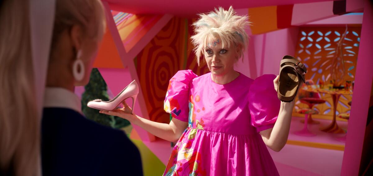 Kate McKinnon wears a puffy-sleeved pink dress and holds a Birkenstock sandal as Weird Barbie.