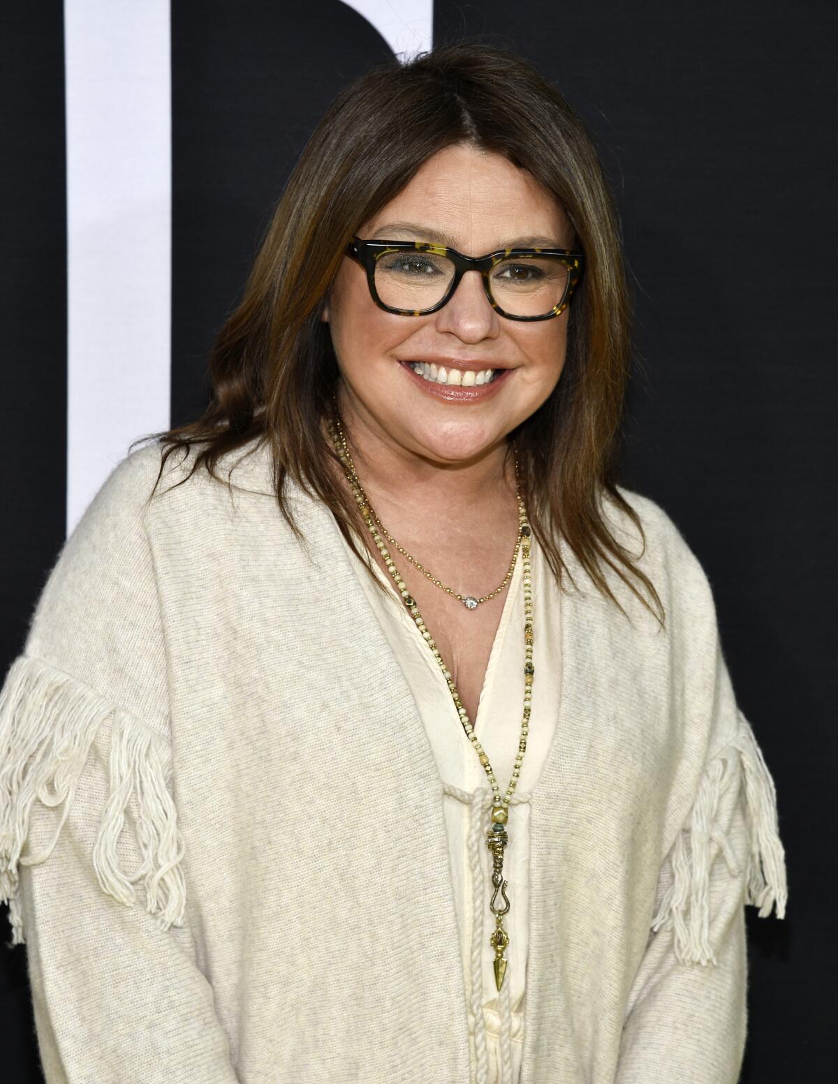 A woman wearing thick black glasses and a white tunic 