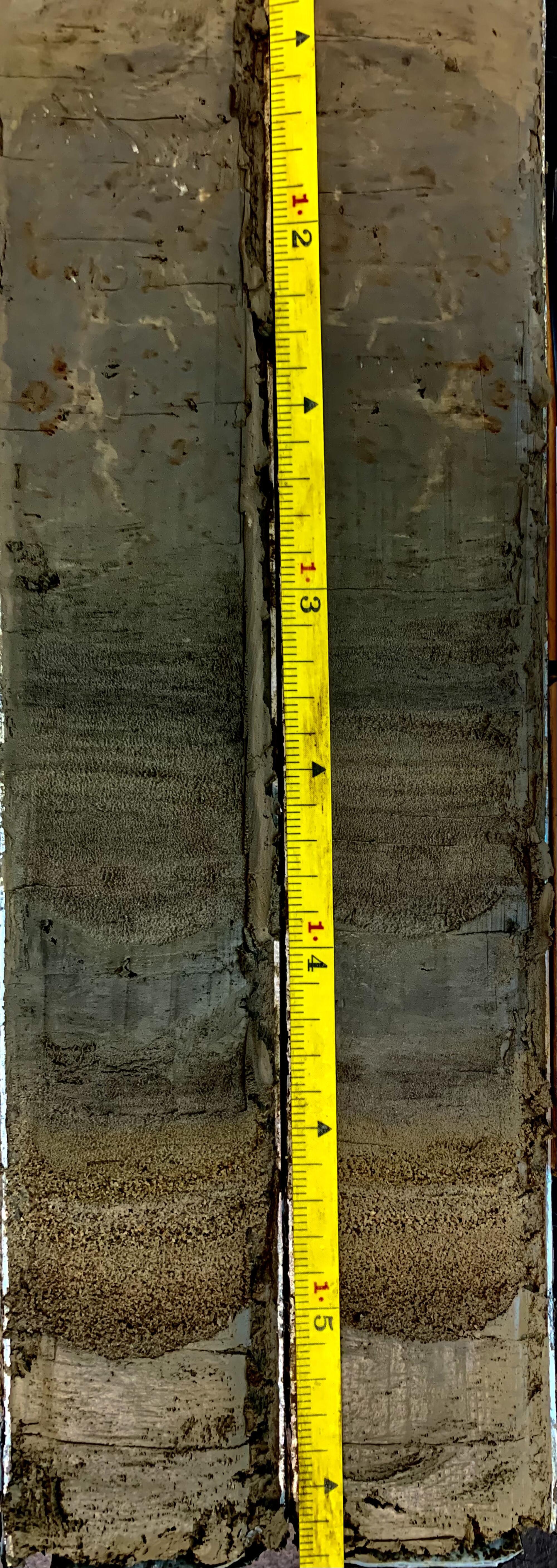 A yellow tape measure next to layers of sediment