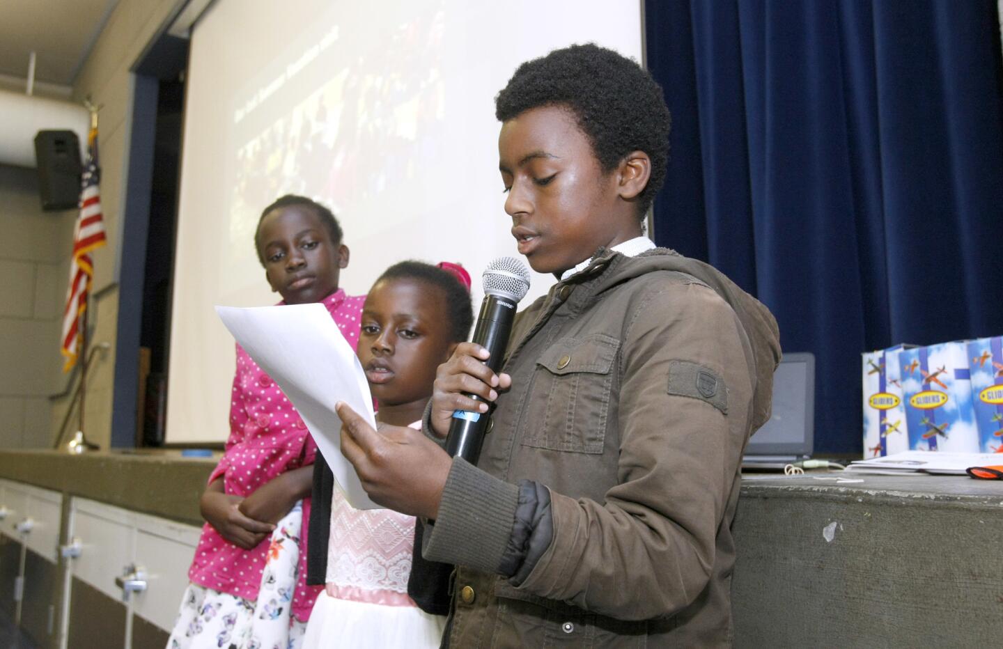 With his sisters fifth grader Ashley Otieno, left, and second grader Nicole Otieno, center, next to him, Palm Crest Elementary School sixth grader Elijah Otieno, right, speaks at school assembly about the family's international philanthropy clothing and school supplies collection, at the La Ca–ada Flintridge school on Friday, March 24, 2017. The three children gave a presentation about their parents' country of origin, Kenya, and also spoke about their effort to collect used clothing and school supplies to take back to Kenya. This will be their second year collecting items for Kenyan children.