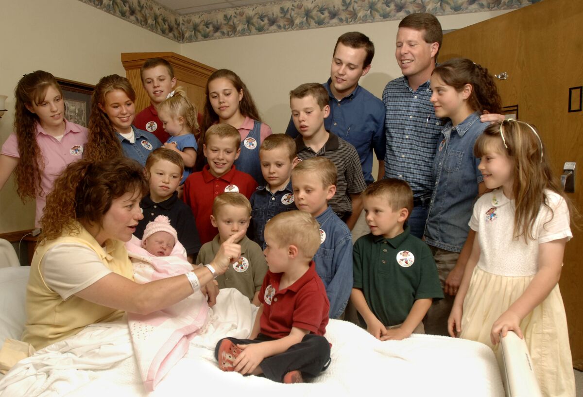 Michelle Duggar is surrounded by her husband and kids as she holds a new baby in a hospital bed.