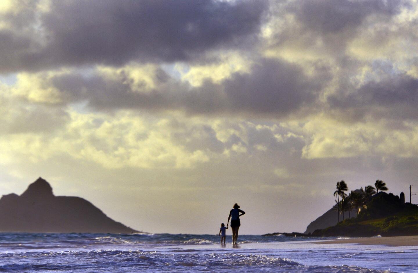 Anne Kllingshirn of Kailua, Hawaii, walks with her daughter Emma, 1, as storm clouds float overhead during the sunrise hours on Kailua Beach Thursday morning.