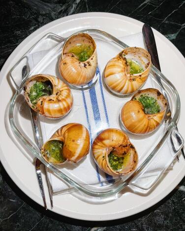Six in-shell escargots on a clear glass tray atop a white plate with white-and-blue napkin at Le Champ