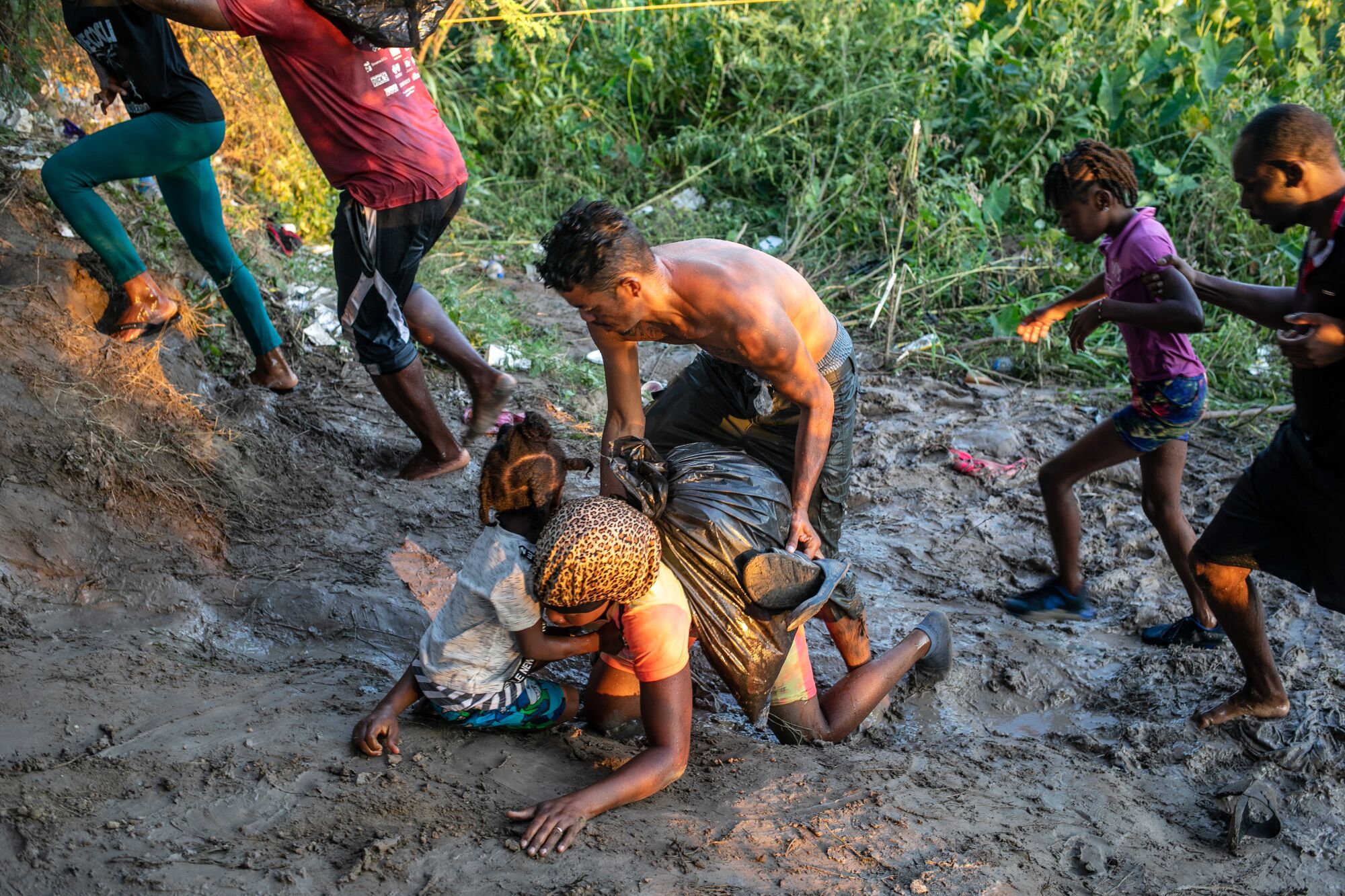 A Haitian immigrant falls in the mud after wading across the Rio Grande and back onto Mexico's shore.