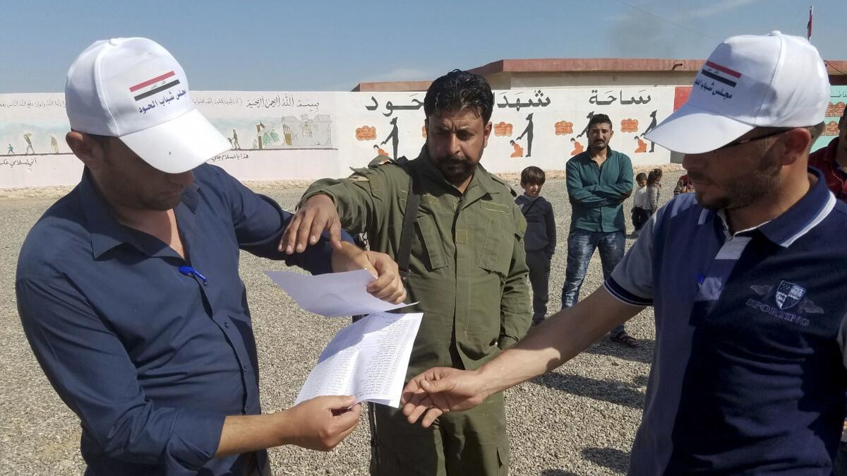 Adil Amash, left, and Hussein Hassan, who have been digging at the mass grave to try to find missing relatives, show Sunni militia member Sgt. Major Yasser Ahmed a list they have compiled of 118 people missing or presumed dead.