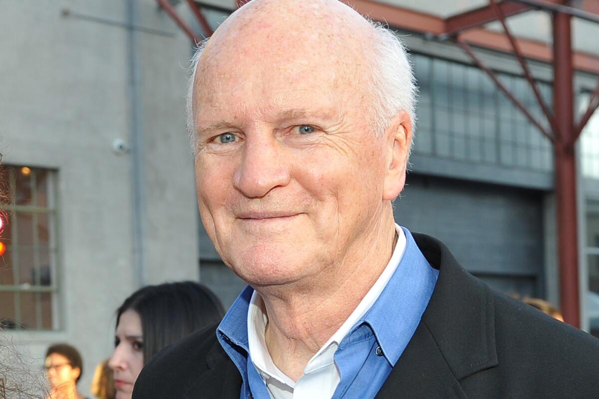 A headshot of a man in a blue button-down shirt and black coat  