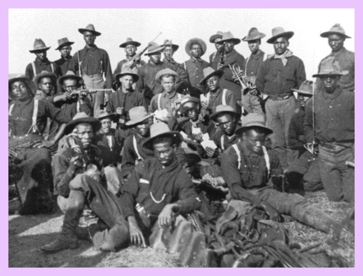 In a black and white photo, a group of Buffalo Soldiers sit and stand for a photo.