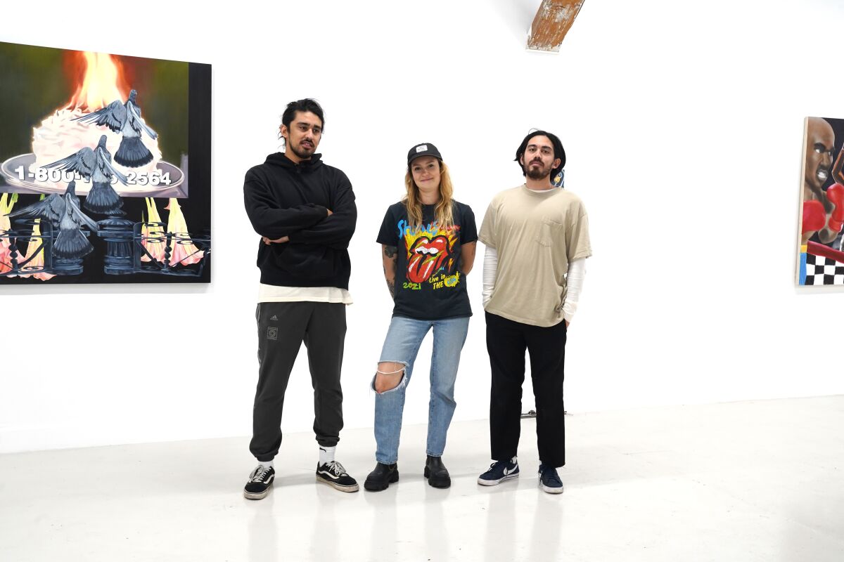 Three people stand next to an artwork hanging on a wall at Good Mother Gallery.