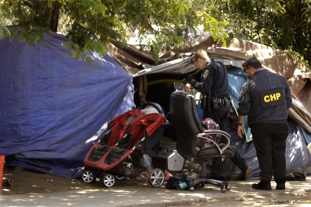 Police offers look inside a tent at a homeless encampment
