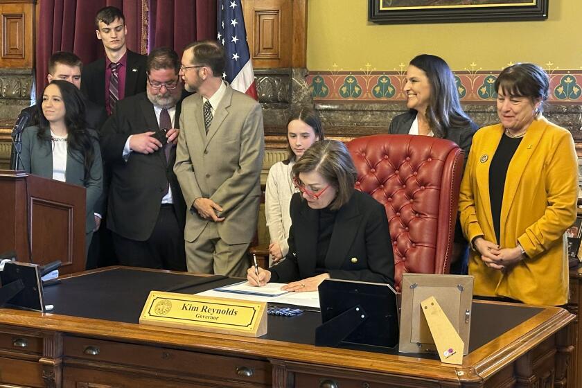 Iowa Gov. Kim Reynolds signs a bill repealing an explicit requirement that Iowa's state, county and local decision-making bodies be balanced by gender, Wednesday, April 3, 2024, in Des Moines, Iowa. Before signing the repeal bill into law, Reynolds said the focus for boards and commissions “should always be on appointing the most qualified people.” (AP Photo/Hannah Fingerhut)