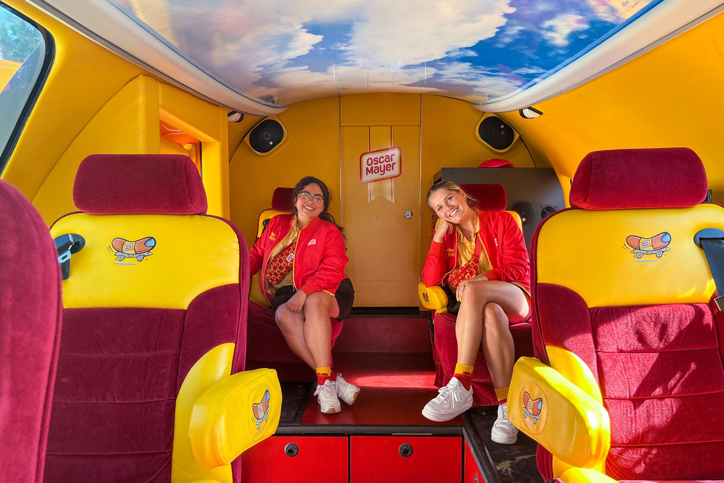Two women sit in the back of a vehicle whose interior is yellow and red.
