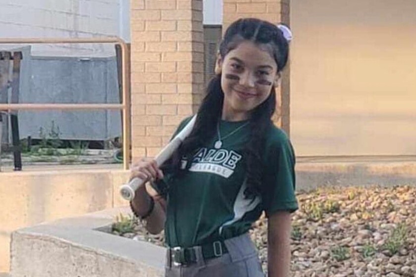 A little girl in a softball uniform, holding a bat
