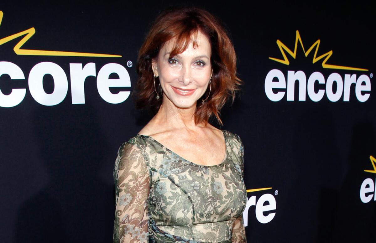Jill Jacobson poses in a patterned green and tan dress with sheer arms