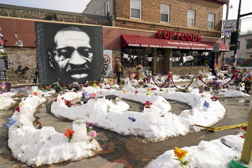 Flowers planted in snow surrounding a black-and-white mural of George Floyd