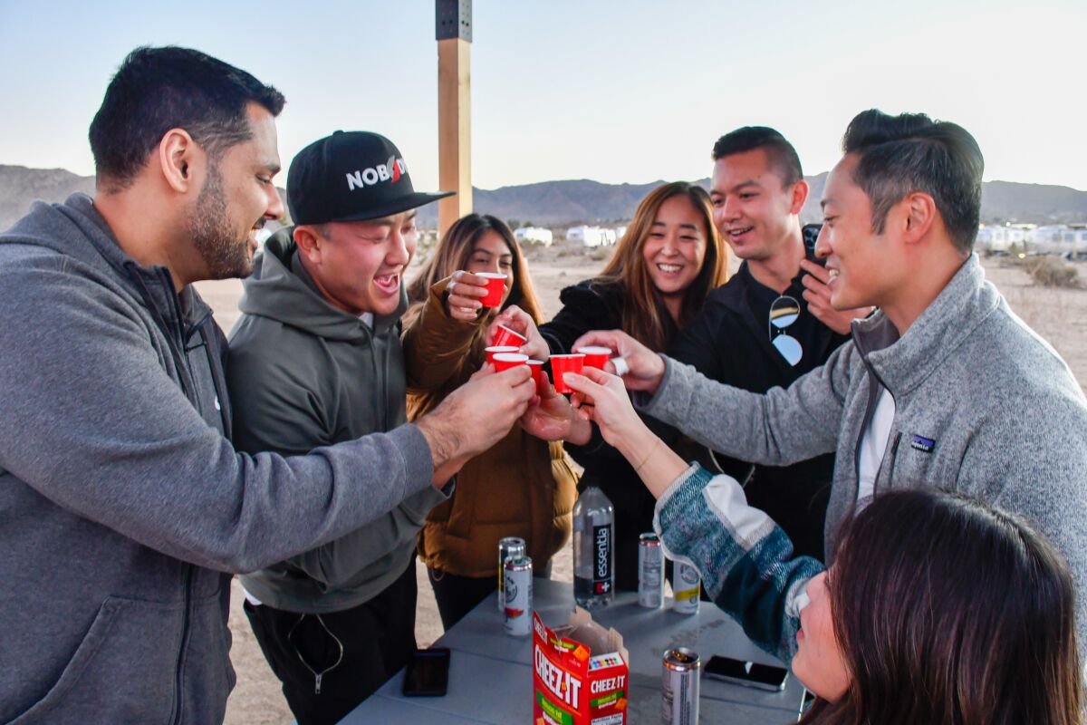 Seven people cheers with small red cups.