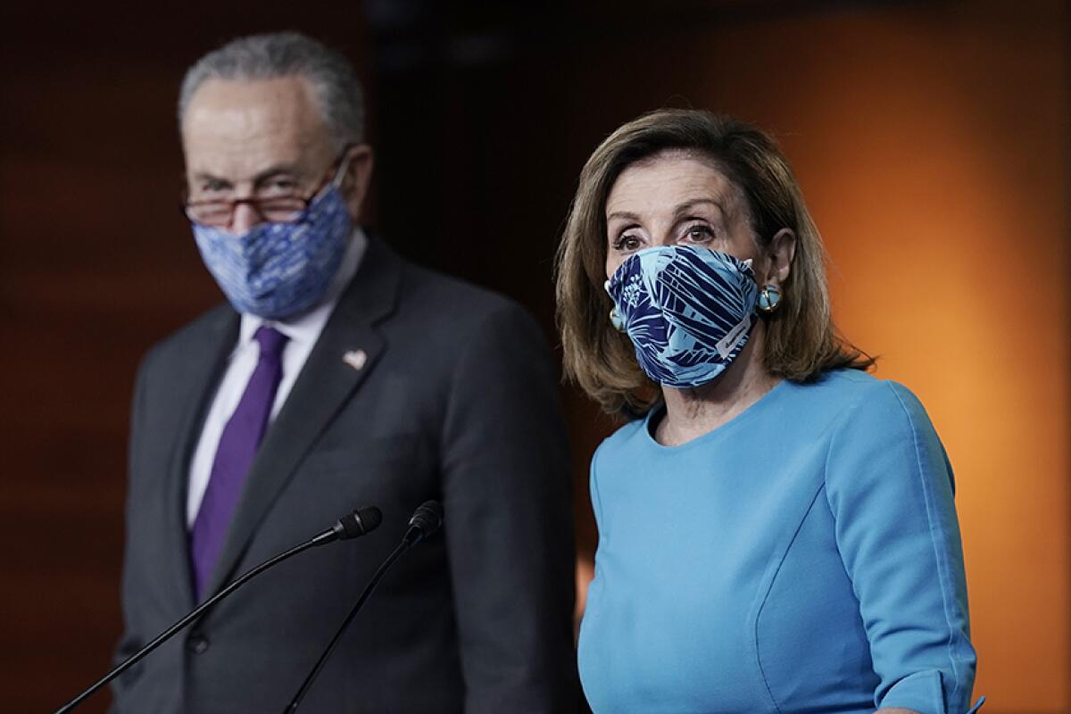A man in glasses, wearing a mask, dark suit and purple tie, left, next to a masked woman in a blue top 