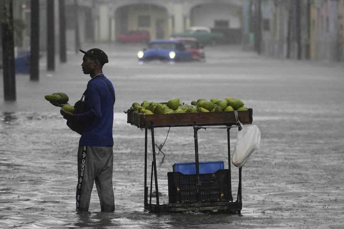 A man stands ankle-deep in a flooded street next to a fruit stand.