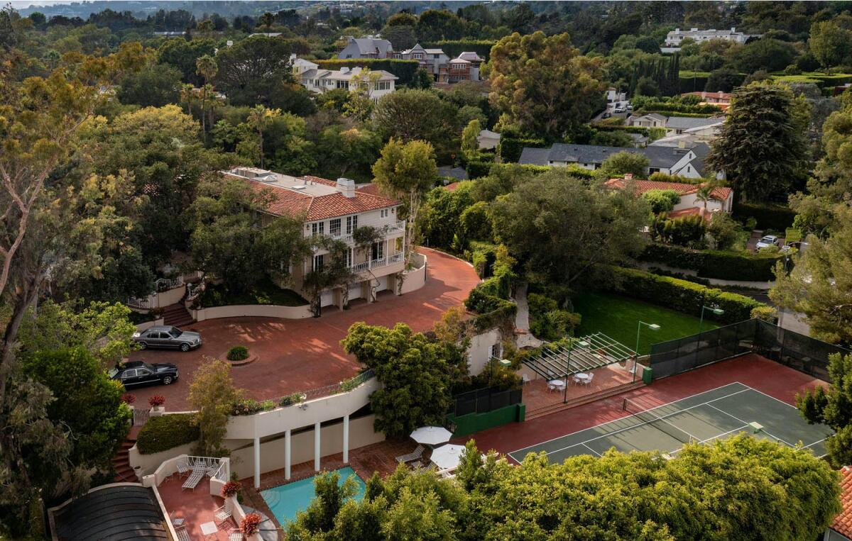 An aerial view shows a mansion, a large motor court, a pool and tennis court.
