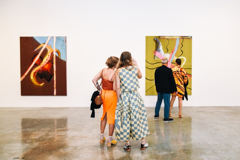 Four people look at two paintings in a gallery.
