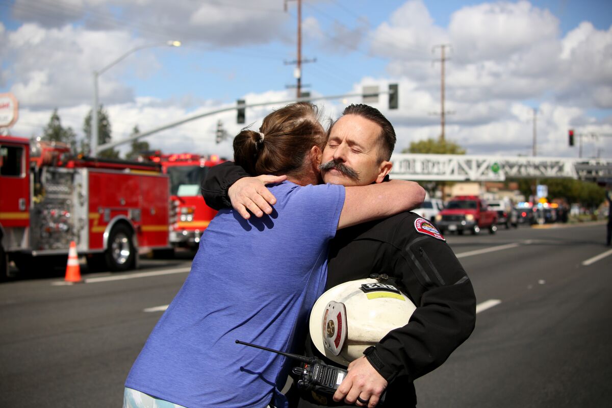 A woman in a T-shirt hugs a firefighter in uniform