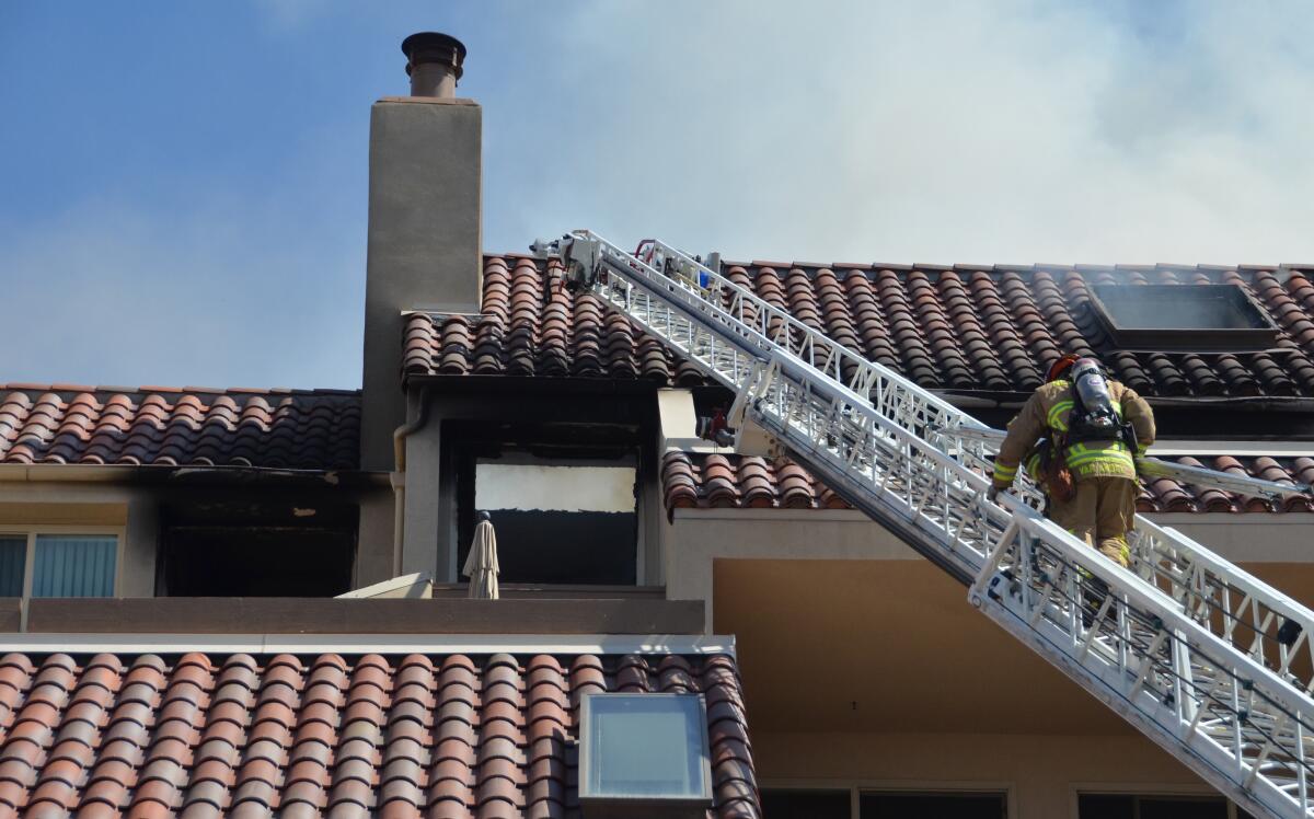 A firefighter scales a ladder at apartment fire in Newport Beach.
