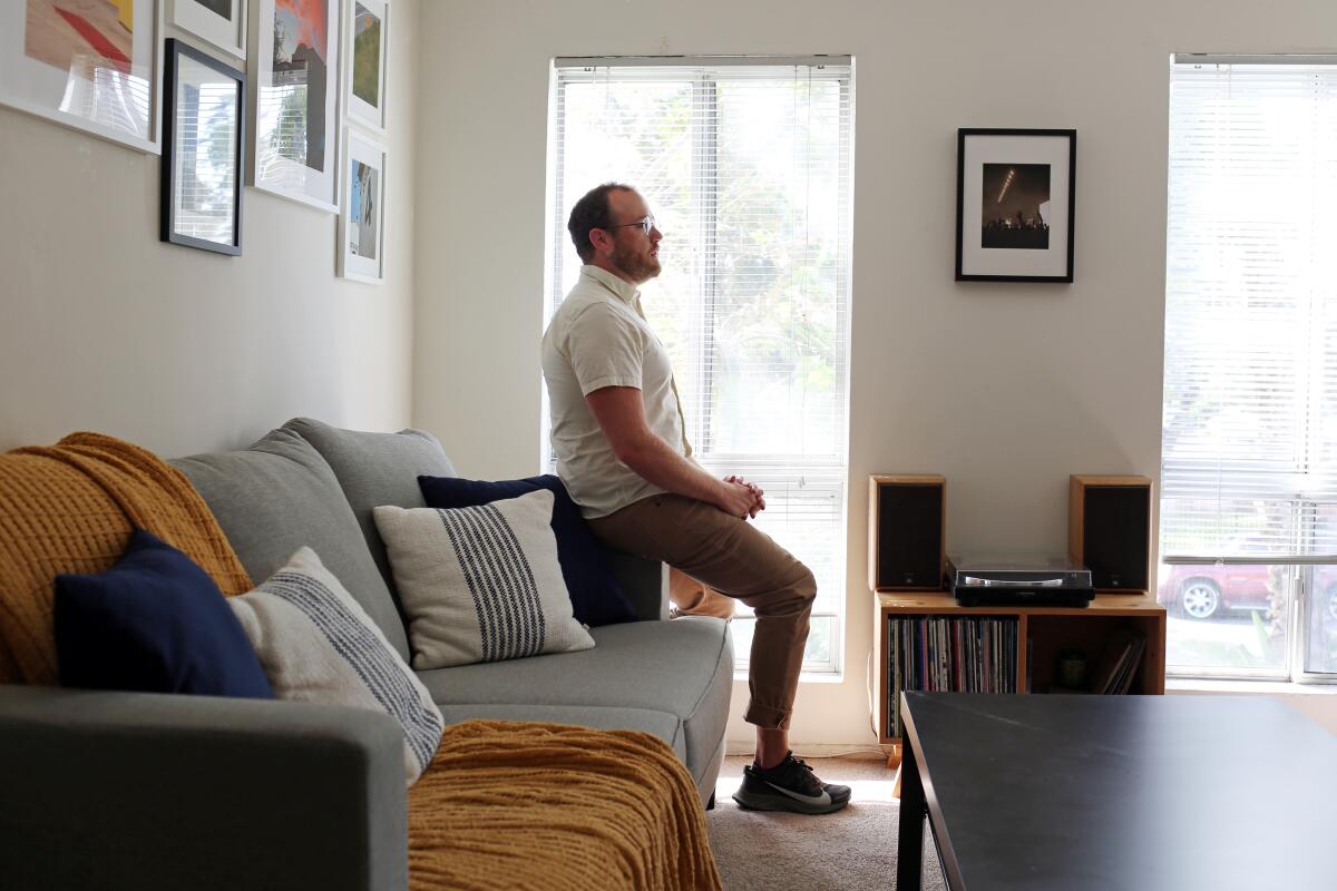 A man sits on the arm of a living-room couch.