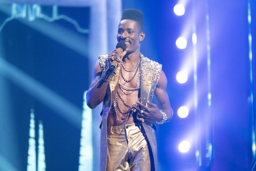 A man in a gold pants and vest combo on stage holding a microphone