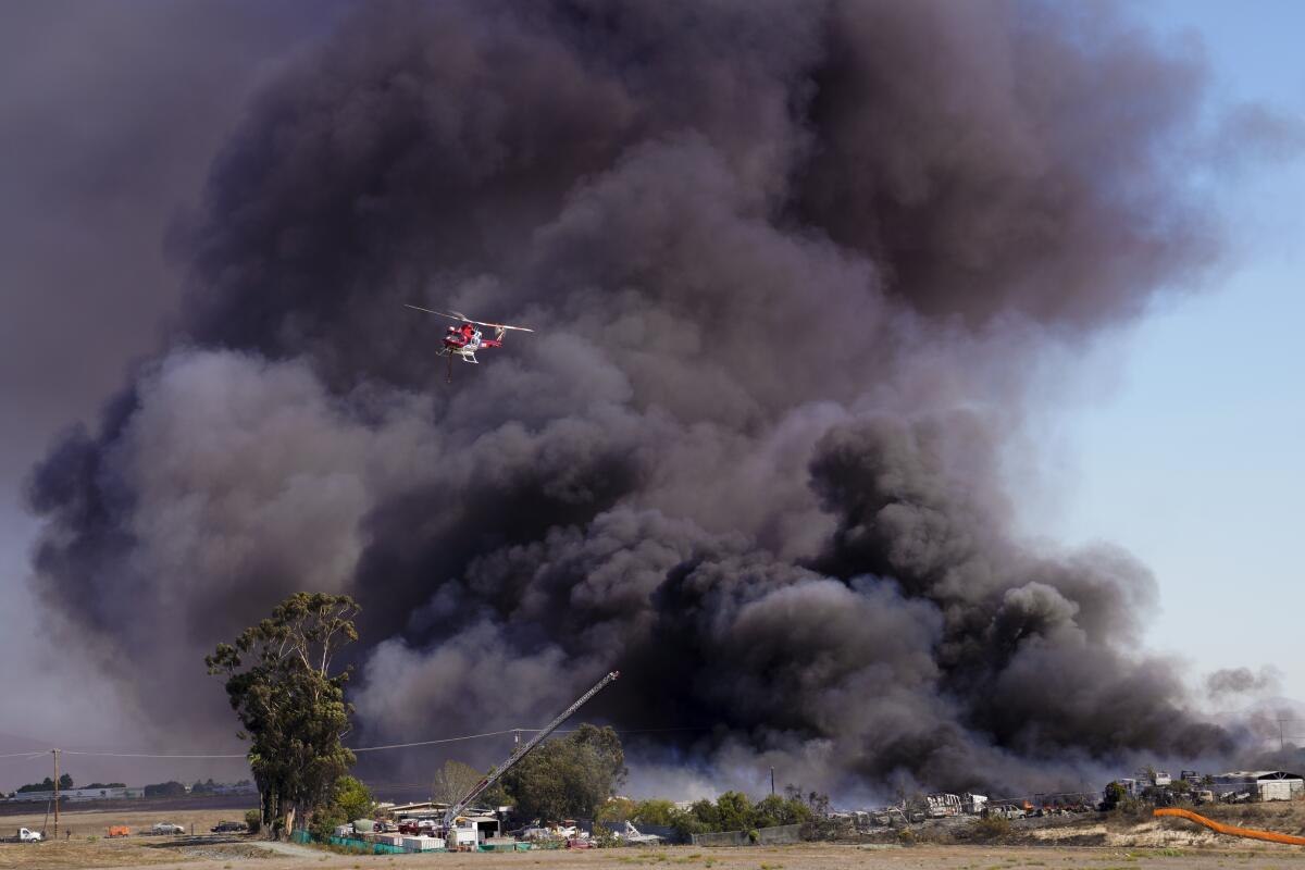 A helicopter flies near black plumes of smoke