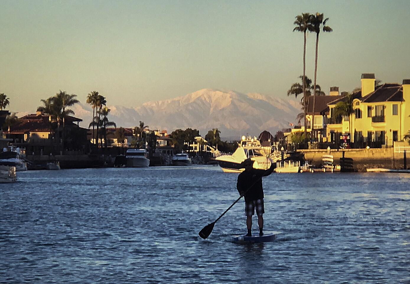 A stand up paddleboarder takes in the view of snow-capped San Gabriel Mountains while cruising through Huntington Harbour