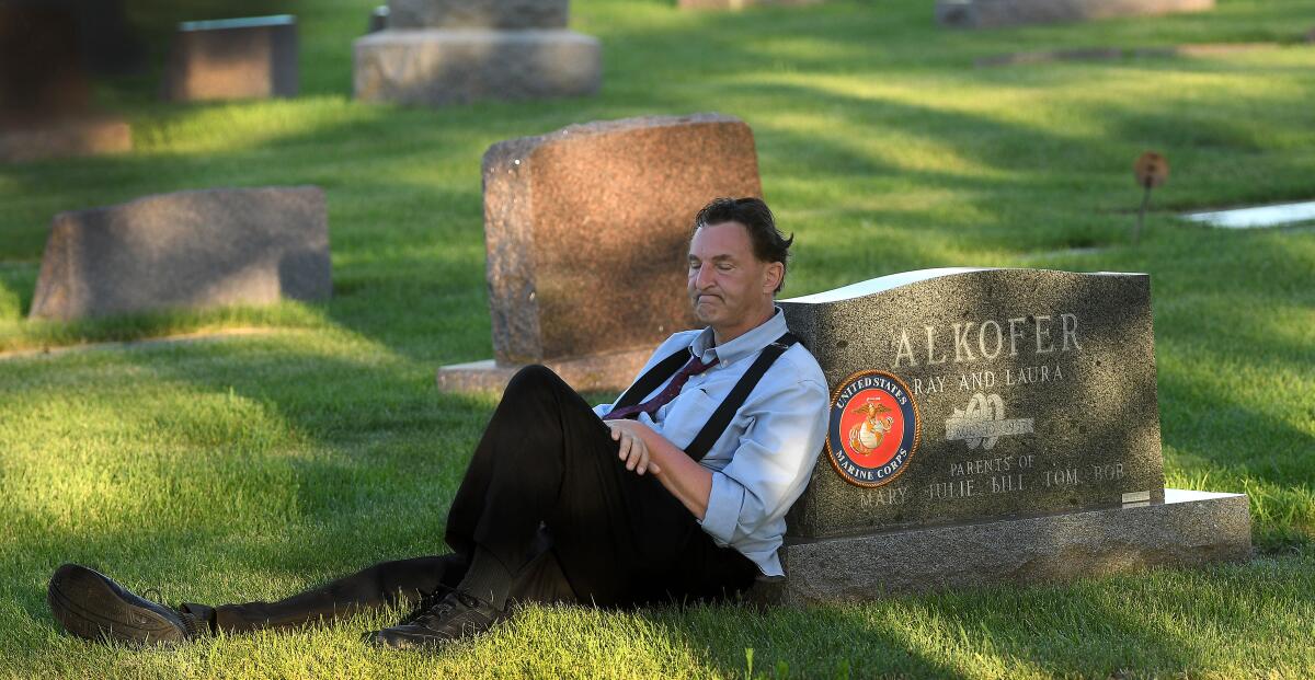 Bill Alkofer leans against his father's tombstone during a visit on the Fourth of July 2020. 