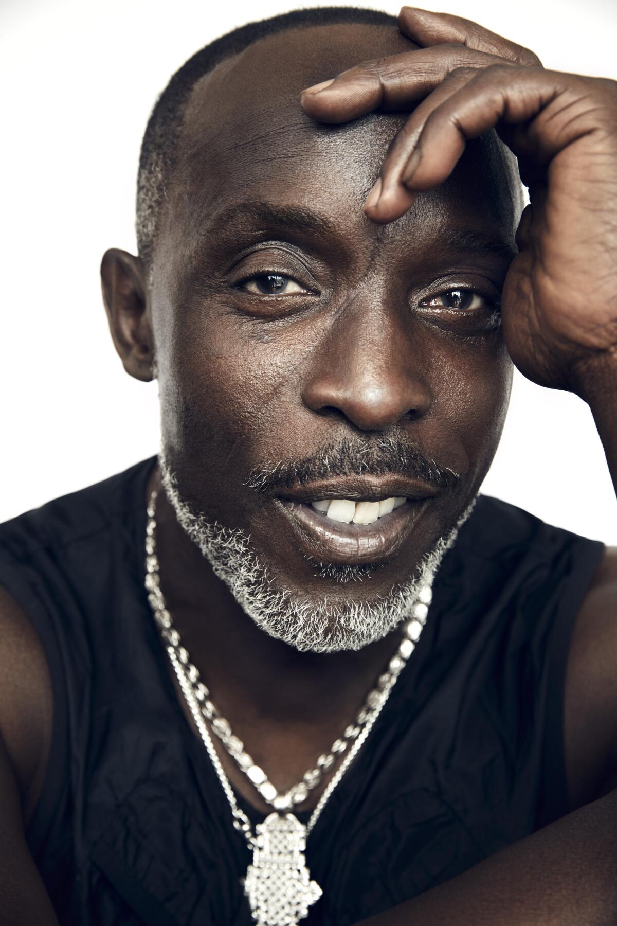 Michael K. Williams, with a bright silver chain around his neck and a hand on his head.