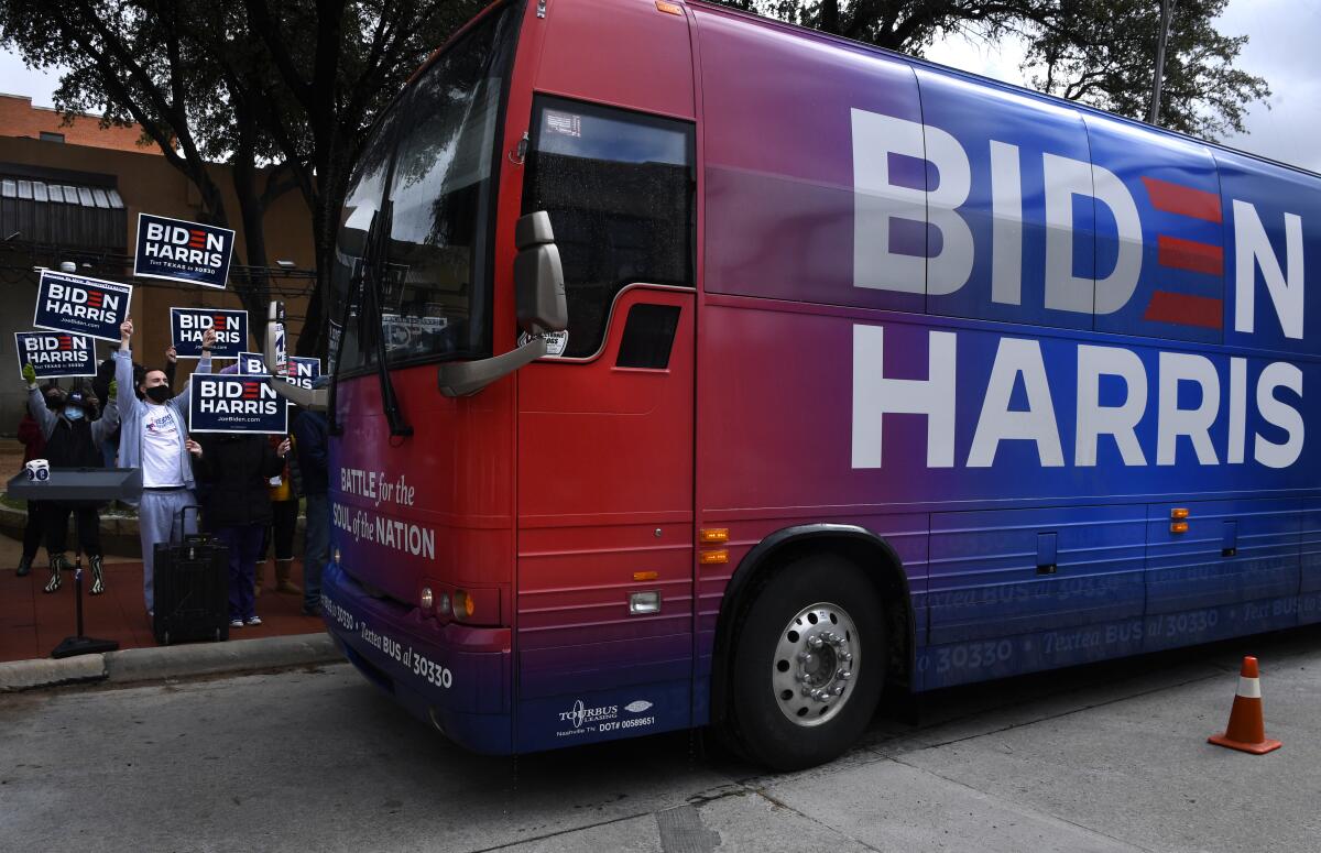 Biden-Harris campaign bus in front of people holding banners.