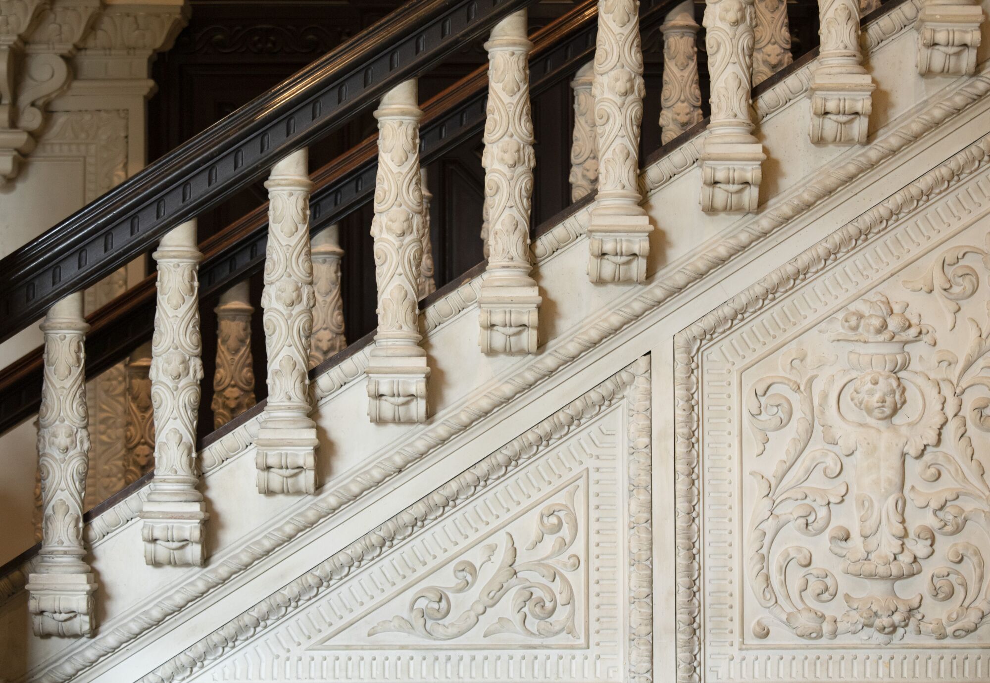 A detail shot of a marble staircase shows ornate reliefs of flowers and leaves and an angel bearing a basket of fruit