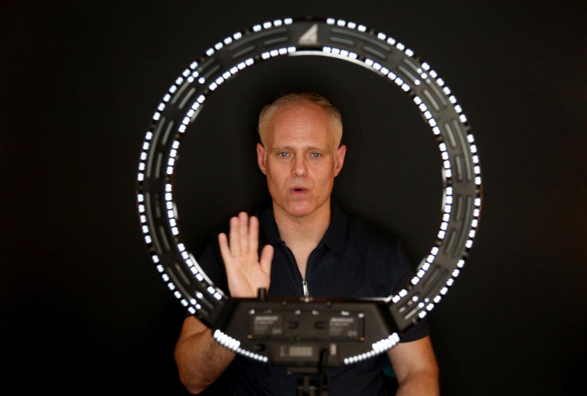 A man encircled by a ring light, with one hand raised