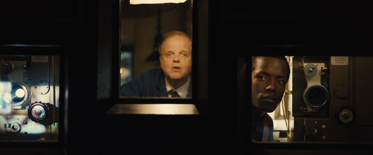 Two men look through windows of the projection booth into a movie theater in "Empire of Light." 