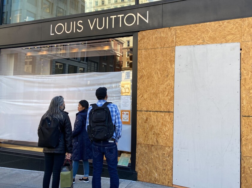 Los visitantes de Union Square observan los daños en la tienda de Louis Vuitton el domingo 