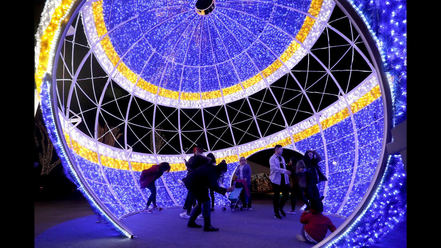 Visitors take photos inside a giant Christmas tree ornament during Winter Fest OC at the OC Fair & Event Center in Costa Mesa on Thursday evening. On New Year’s Eve, Winter Fest will feature a ball drop and a countdown to fireworks at both 6 p.m. and midnight