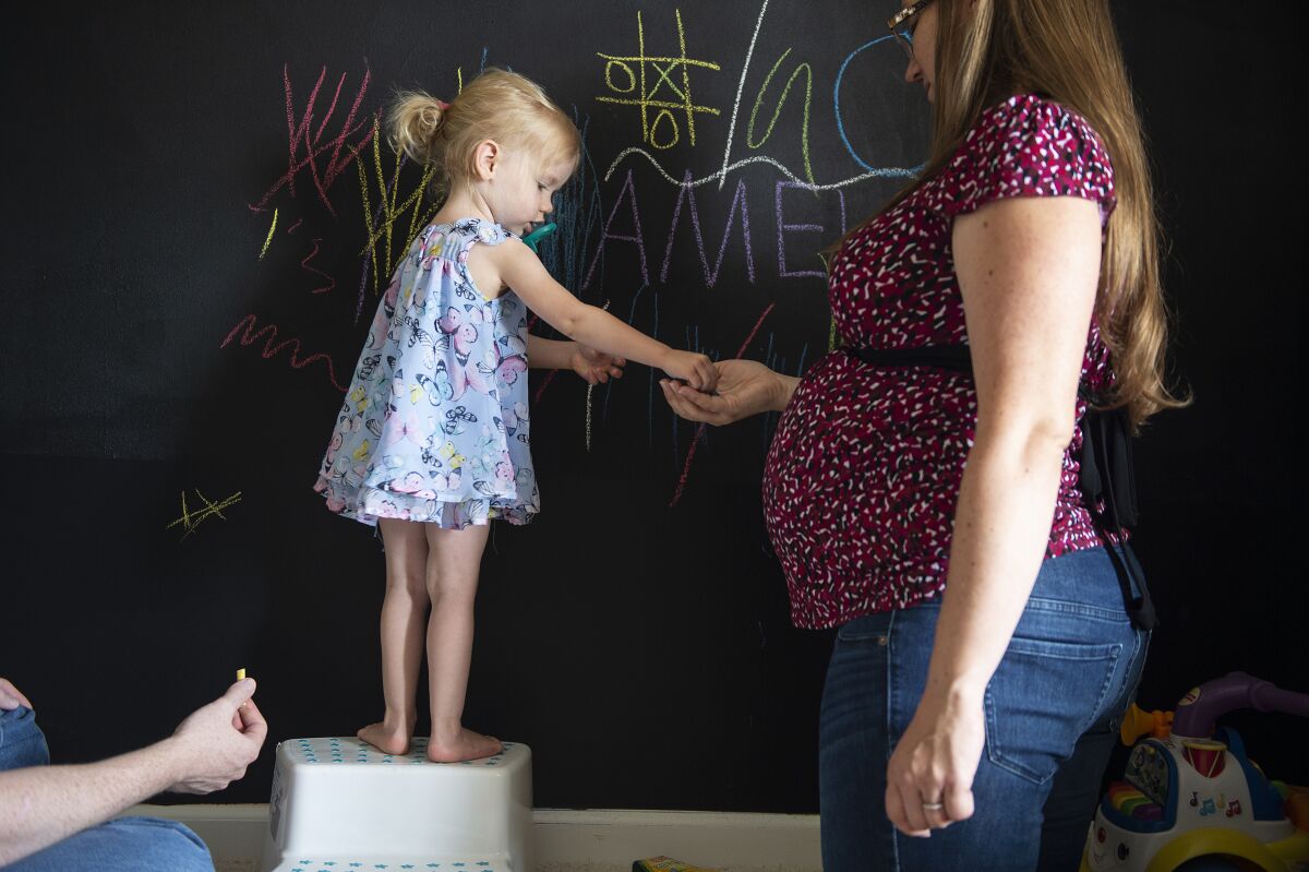 Rebecca Grimm plays chalk with her 2-year-old daughter, Amelia, and husband, Mark, at their home in Westfield, Ind.