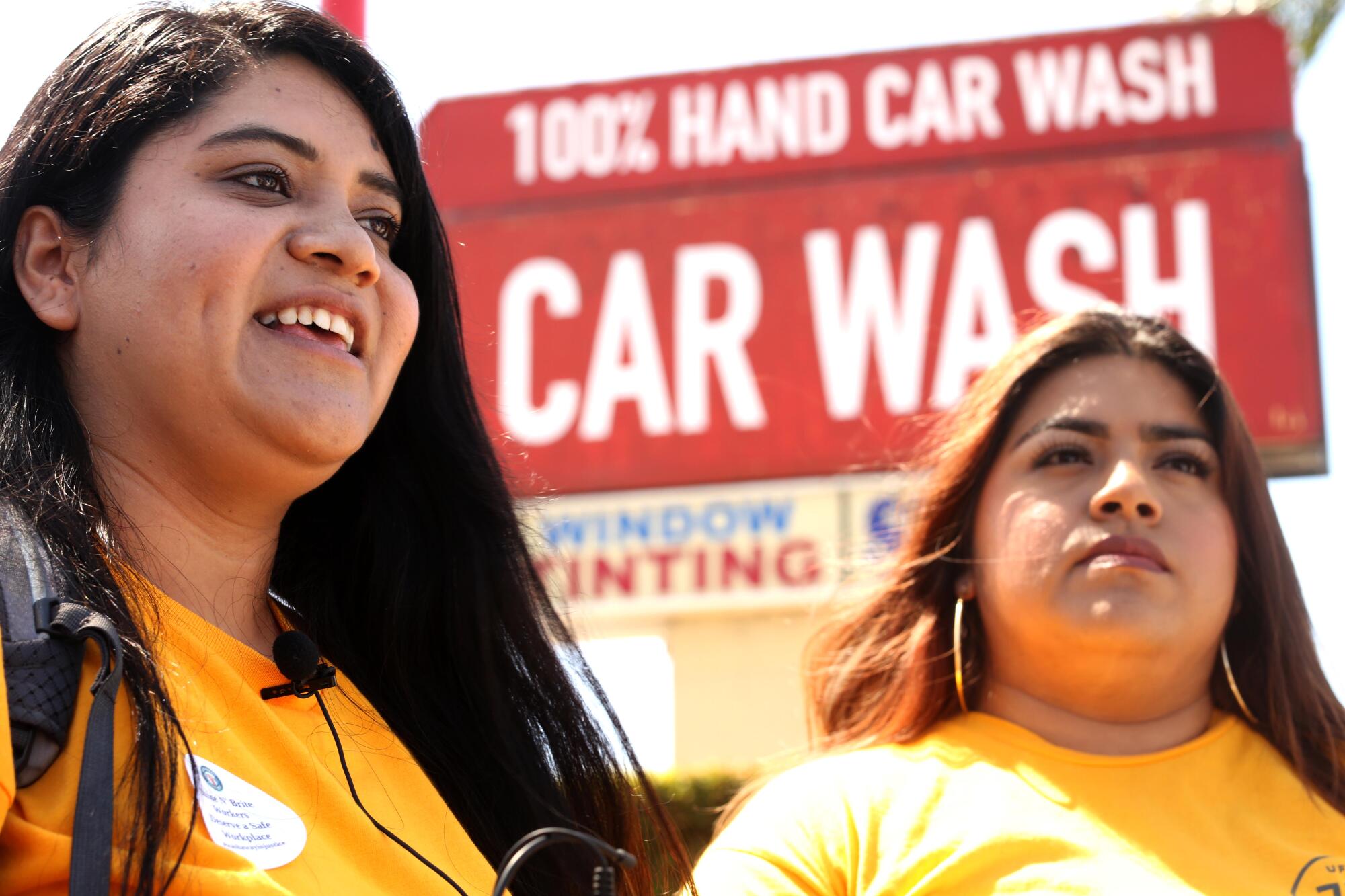 Two female UCLA students stand outside with a carwash sign in the background.