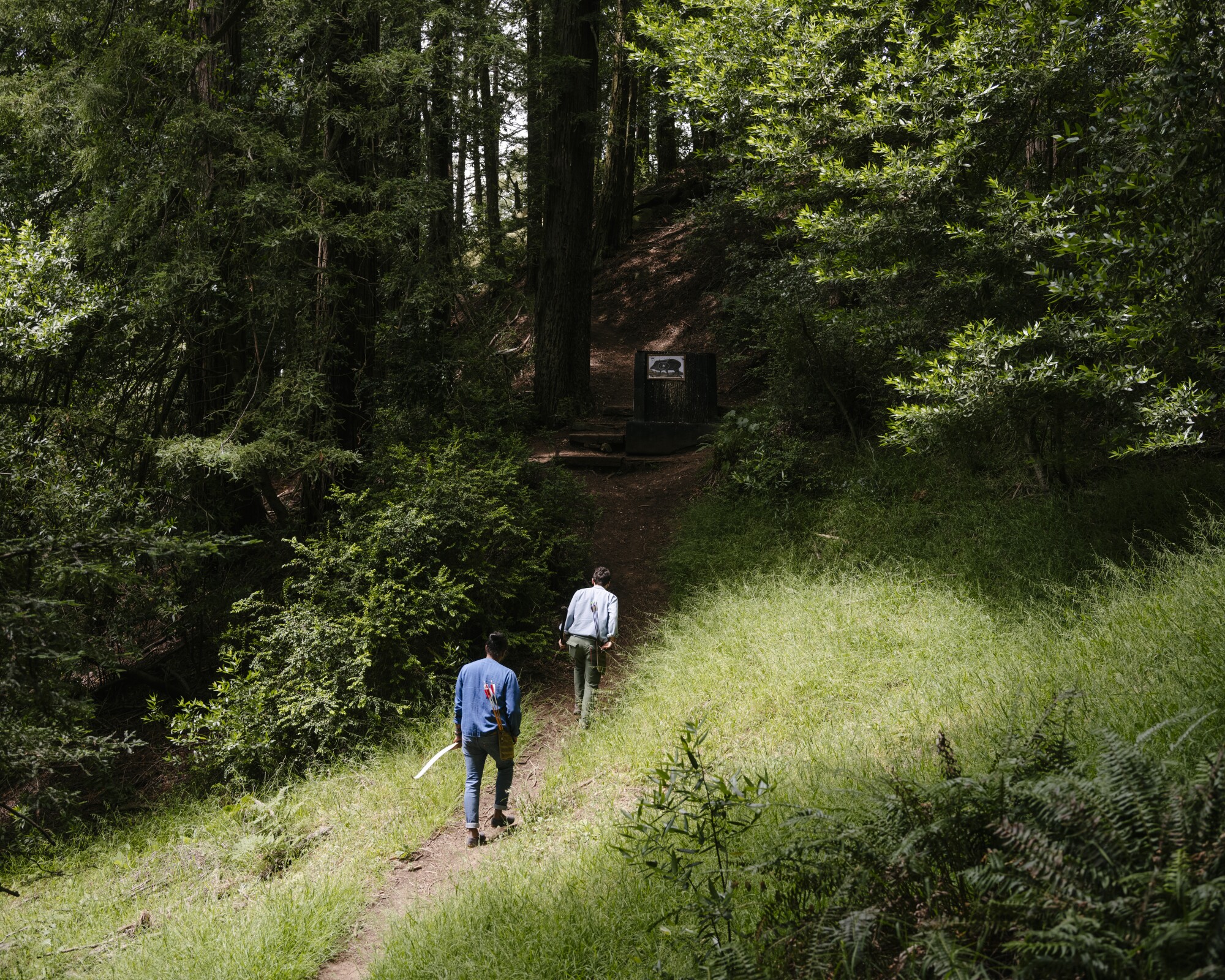 Deux hommes portant des arcs et des flèches marchent le long d'un sentier.