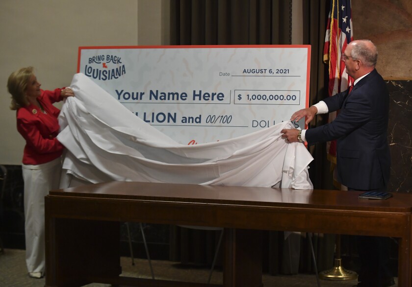 First lady Donna Edwards, left, and Gov. John Bel Edwards, right, unveil a giant check during a news conference at the Louisiana State Capitol in Baton Rouge, La., on Thursday, June 17, 2021, to announce that Louisiana will participate in a lottery, giving cash prizes and scholarships to residents who have been vaccinated against the coronavirus. (Hilary Scheinuk/The Advocate via AP)