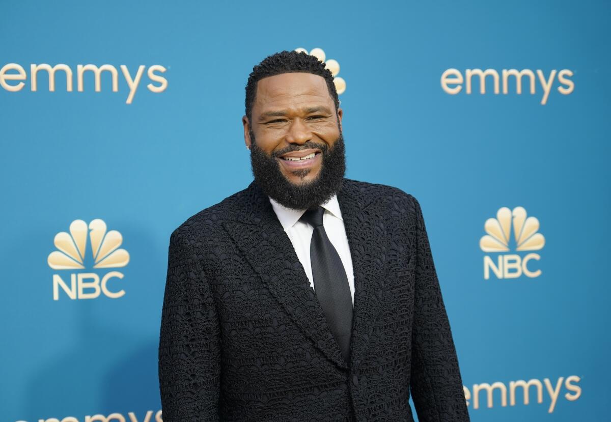 Anthony Anderson in a black suit and tie stands in front of a blue backdrop with the NBC and Emmys logos on it.